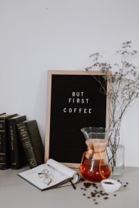 livros, jarra de chá e uma lousa escrito BUT FIRST COFFEE