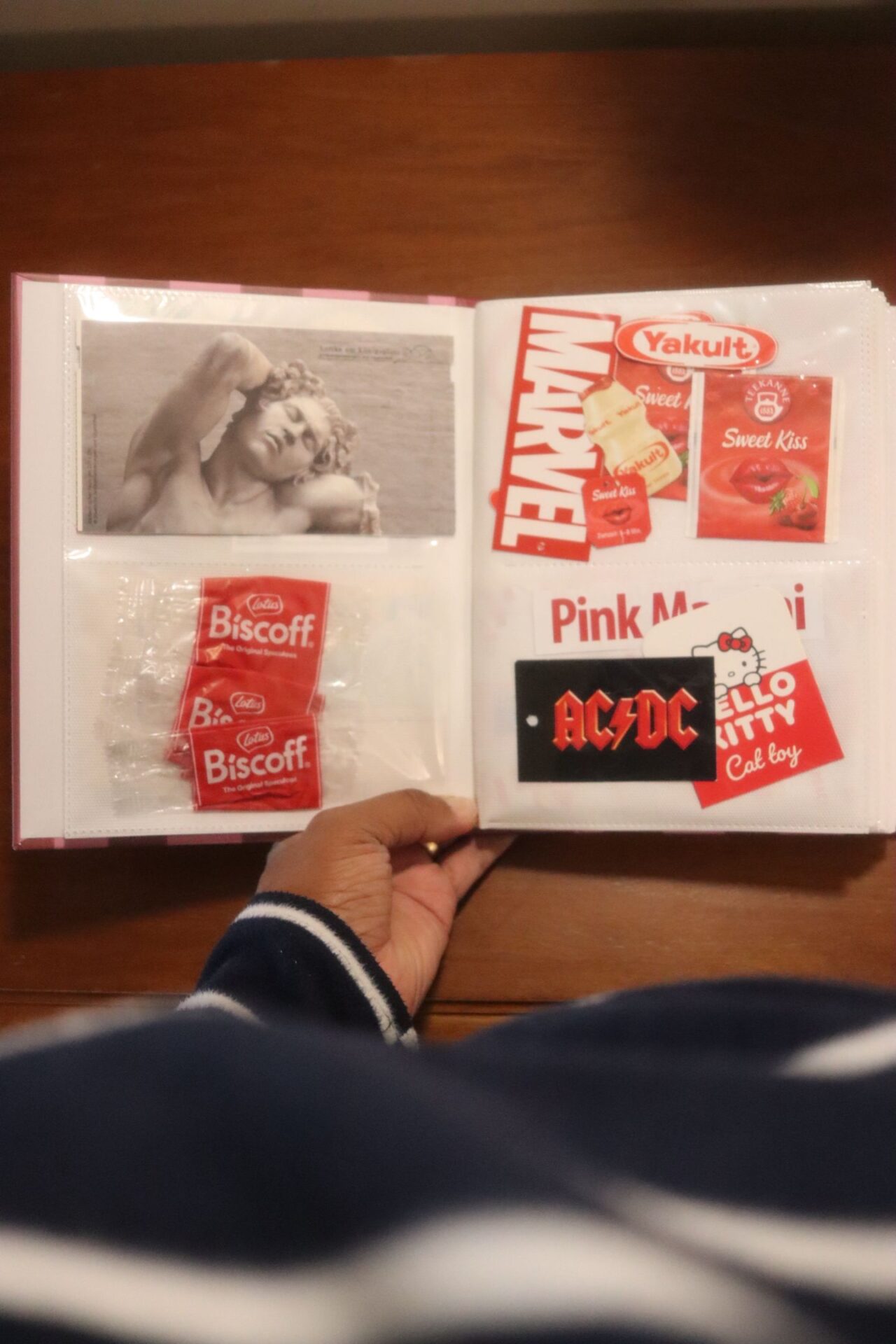 Página vermelha do álbum de recortes com embalagens de Biscoff, Yakult, chá Sweet Kiss e cartão-postal de escultura